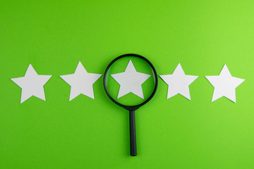Rating concept. 5 stars with a magnifying glass. White stars on a green background