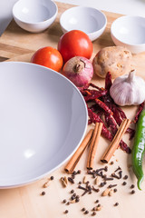 Empty white bowl with assorted vegetable and spices ingredients as foreground.