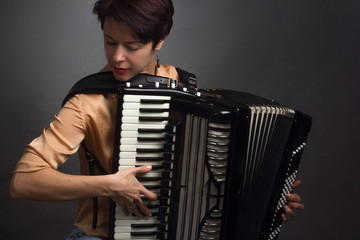 A brunette in a gold shirt, with short haircut, on a light gray background of the Studio. With accordion musician
