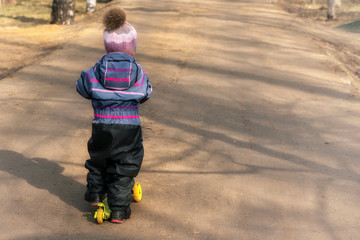 Fototapeta premium child 4 years old rides a yellow scooter on a dirt road in a city park