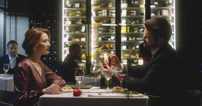 Caucasian young handsome man proposing to his pretty girlfriend in restaurant while couple eating desert with wine. Boyfriend making offer to girlfriend and giving ring. Romantic date concept.