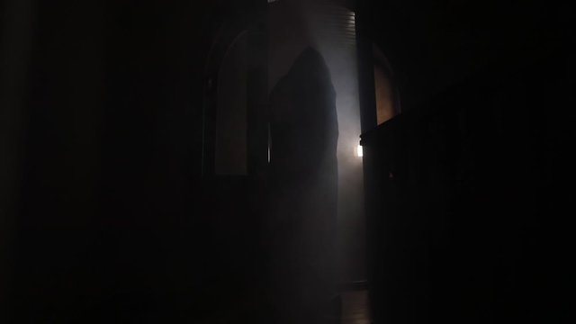Silhouette of an unknown shadow figure on a door through a closed glass door. Spooky silhouette girl at night with smoke in background