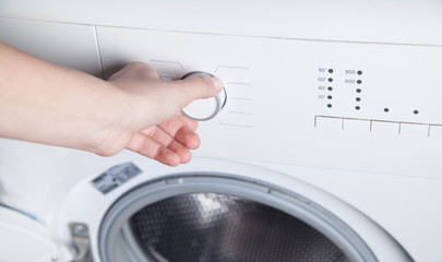 Girl hand is turning knob of washing machine.