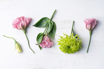 Pretty flower arrangement including pink lisianthus and green chrysanthemums, on a rustic white wooden background, photographed from above.