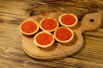 Tartlets with red caviar on a wooden table