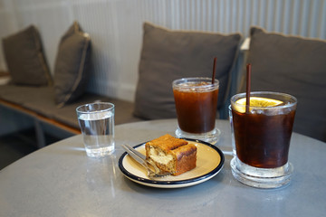 Glasses of iced black coffee and spring water served with bread pound cake filled with custard cream
