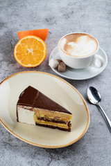 A slice of peach mousse cake in a chocolate glaze on a white wooden table in a restaurant