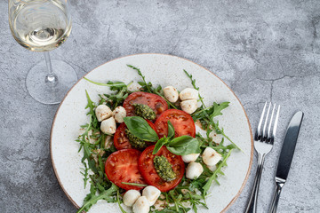 Caprese salad with ripe tomatoes, mozzarella cheese and pesto sauce on grey stone table