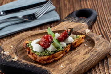 Bruschetta with sun-dried cherry tomatoes, mozzarella and pesto sauce on crunchy toasted ciabatta. Served on rustic cutting board
