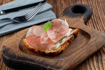 Bruschetta with sliced prosciutto and rich cream cheese on toasted ciabatta on wooden cutting board