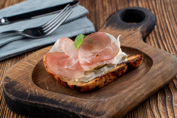 Bruschetta with sliced prosciutto and rich cream cheese on toasted ciabatta on wooden cutting board