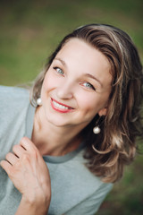 Fototapeta premium Stock photo headshot of an attractive young woman with dyed middle length hair with red lips and earrings smiling at camera with happiness. Blurred background.