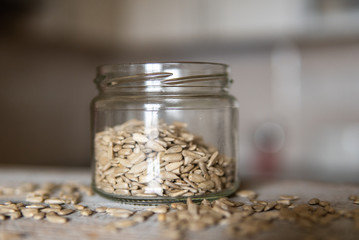 Sunflower seeds in a jar and scattered seed on the white vintage table with a kitchen on background. Healthy vegetarian protein nutritious food. Sunflower seed on rustic old wood.