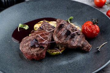 Beef tenderloin medallions with mulled wine sauce with grilled vegetables on black plate