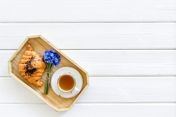 Fototapeta na wymiar Breakfast with summer flowers. Tea, croissant and cornflowers on white wooden background top-down copy space
