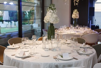 round served table with tablecloth with plates, glass, fork and knife. festive table in restaurant decorated vase of vivid beautiful flowers on the birthday on wedding party. 