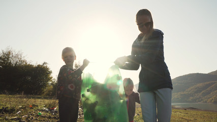 Young mother and her daughters carry a green bag full of trash counter light