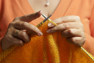 Female hands knitting with needles from yellow wool.