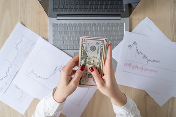 Time lapse. Woman freelancer holding banknotes fifty U.S. dollars in hand and counting profit, income. laptop with graphics and charts printed on the paper on office table. Flat lay