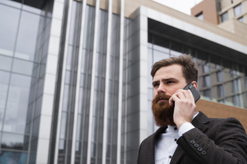 Businessman talking on the phone in financial district. Portrait of a Young urban professional man using smart phone over office building. Business man talking on his smartphone outdoors. Technology.