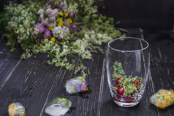 Flowers of bedstraw and cherry fruits with a transparent glass on the table with ice