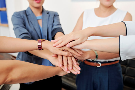 Close-up image of female entrepreneurs stacking hands to express support before starting work on big project