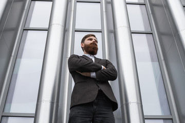 Portrait of an handsome businessman wearing jacket over office building in financial district outdoors. Young bearded Businessman outdoor. Successful entrepreneur dressed in formal wear.