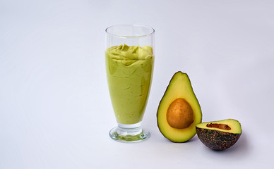 A glass of avocado and spinach smoothies and half an avocado on white background. Fitness product. Dietary sports nutrition.