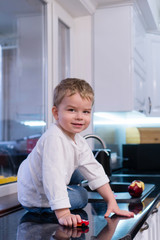 Obraz premium Portrait of happy joyful beautiful boy in kitchen background. Child eats an apple, rolls a toy car on the table and enjoys life. happy and carefree childhood. Healthy eating concept.