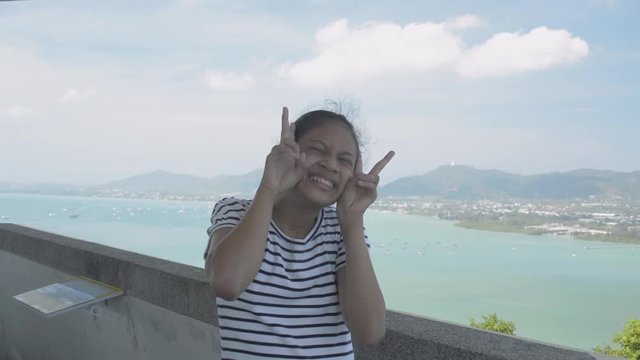 Asian cute girl in casual dress taking her picture with funny posing on view point tower with stunning scenery during summer.
