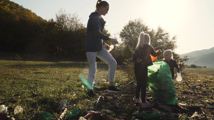 little toddler girl picking up trash with her mother and sister