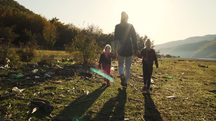 Ecological issue: mother walking with her daughters on land full of garbage