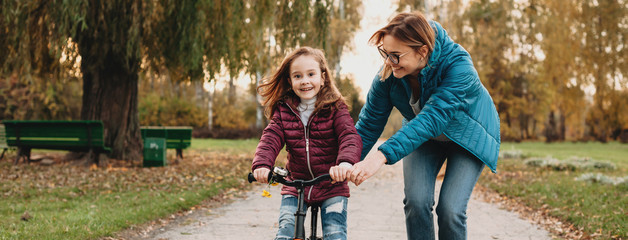 Cheerful middle aged woman is having joy with her girl while she is learning to ride the bike