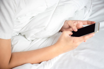 Close up of an Asian hand using a smartphone on the bed in the room.