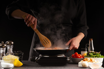 Chef fries seafood, shrimp in a pan. Against the background of vegetables. Black background, cooking and recipe book, cooking and healthy eating.