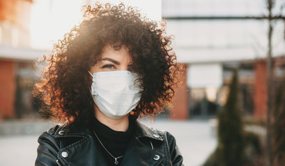 Curly haired caucasian girl is trying to prevent a flu and is wearing a white protective mask