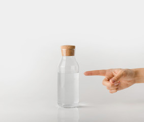 A hand points a finger at a glass bottle of clean water.