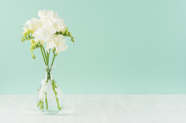 Fresh delicate white flowers freesia in glass vase  in green mint menthe interior on white wood...