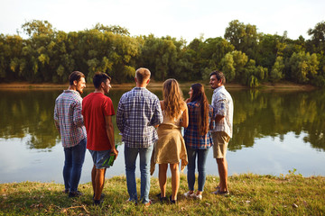 Back view a group of young people resting, communicates on the lake