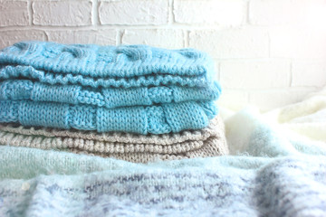 A stack of knitted blue and beige scarf, lies on a mohair plaid and the background is a white brick...