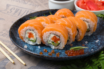 Philadelphia rolls with salmon, avocado, flying fish caviar and Cream Cheese inside on a blue plate.