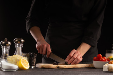Chef cook slicing olives. Against the background of vegetables. Cooking, tasty and wholesome food.