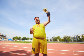 A fat man with a winner's cup in his hands at the stadium.