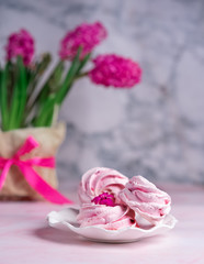 sweet pink marshmallows on a plate with a vase of spring flowers on the table against the background of gray marble. Morning coffee, girl’s breakfast, spring mood