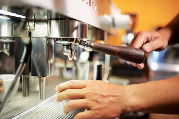 Close-up image of barista putting tamper in coffee machine when brewing drink for customer