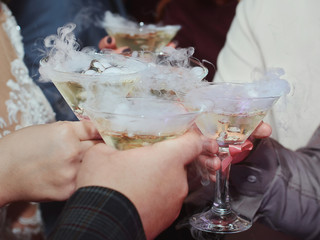 Closeup of hands of people with wine glasses at event, wedding, party. Family and friends clinking glasses and cheering with alcohol. Cocktails with ice vapor