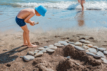 little baby boy playing on the beach by the sea in sand and stones. Build sand castles.