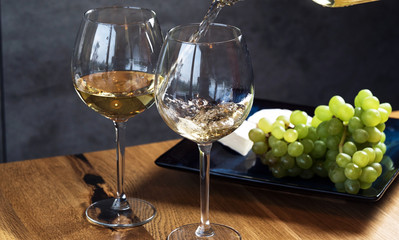 Pouring white wine from bottle into the wineglass on the table