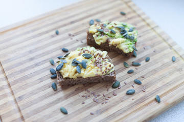 whole grain toast with avocado and flax and pumpkin seeds on a wooden board