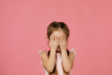 Cute little child girl closes her eyes with her hand on pink background. I see nothing